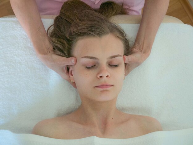 Le mani del medico sono sulle tempie di una giovane donna Massaggio facciale ravvicinato