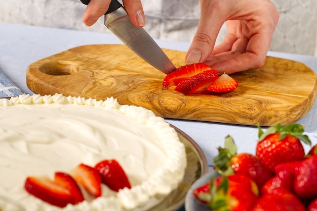 Le mani del panettiere della donna tagliano le fragole per la torta fatta in casa a base di meringa e panna