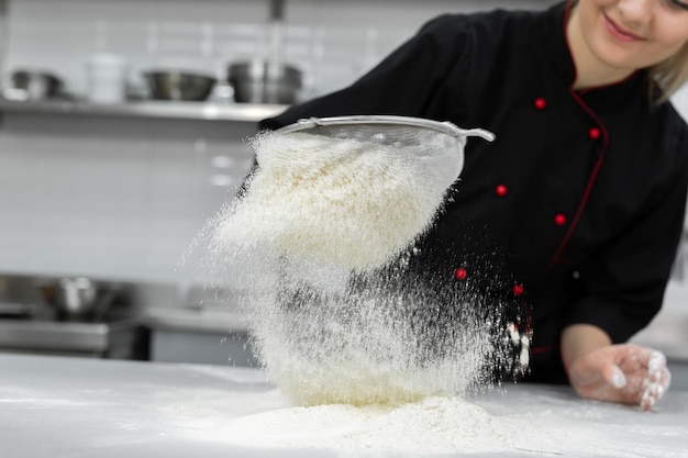 Le mani del pasticcere setacciano la farina attraverso un setaccio sul tavolo.