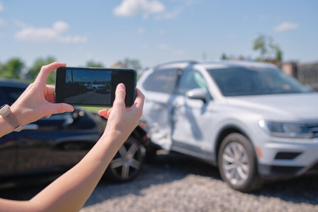 Le mani dell'autista femminile che fotografano sulla fotocamera del sellphone hanno distrutto i veicoli sul lato della strada per il servizio assicurativo dopo un incidente d'auto. Concetto di sicurezza stradale