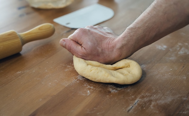 Le mani dell'uomo che impastano pane sulla tavola di legno con il rullo di legno. Concetto di panetteria.