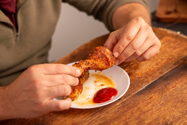 le mani dell'uomo che tengono la coscia di pollo al tavolo