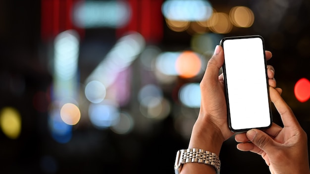 Le mani dell'uomo che tengono schermo vuoto dello smartphone con il bokeh della città di notte.