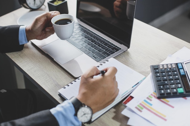 Le mani dell'uomo d'affari che tengono una tazza di caffè e una penna sembrano fare un piano di lavoro o scrivere sul