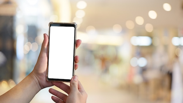 Le mani dell'uomo del primo piano facendo uso dello schermo vuoto del telefono cellulare nel centro commerciale.