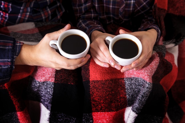 Le mani dell'uomo e della donna tengono due tazze di caffè nel plaid a forma di verme.