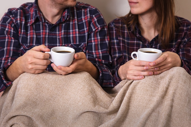 Le mani dell'uomo e della donna tengono due tazze di caffè nel plaid.