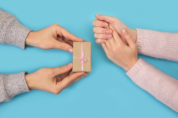 Le mani dell'uomo e della donna tengono la scatola con il regalo sull'azzurro.