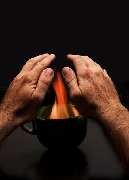 le mani dell'uomo sopra la tazza con il fuoco per riscaldare la povertà energetica