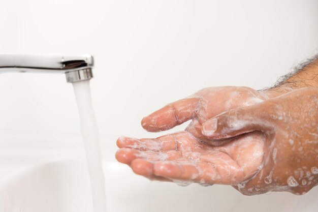 Le mani dell'uomo stanno aprendo il rubinetto di casa e si lavano le mani con acqua pulita e sapone per una buona igiene.