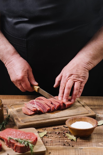 Le mani dell'uomo tagliano le bistecche di carne cruda fresca da vicino