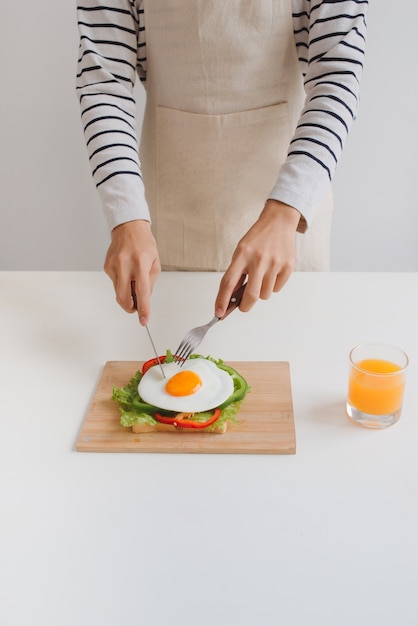 Le mani dell'uomo tagliano le uova su carta, servite con pane, erbe aromatiche, salsiccia e succo fresco.