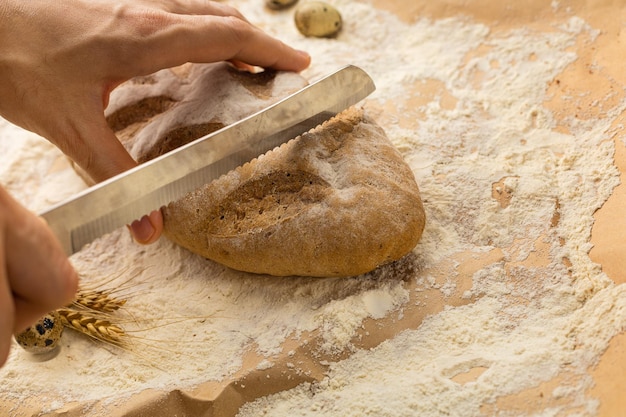 Le mani dell'uomo tagliano un panino di grano fresco con un coltello da pane