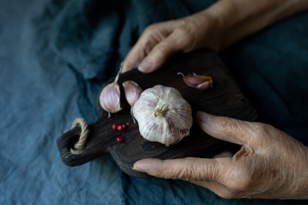 Le mani della donna anziana tengono un tagliere con aglio da vicino