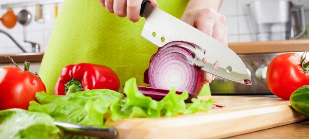 Le mani della donna che tagliano la cipolla del bulbo, dietro le verdure fresche.