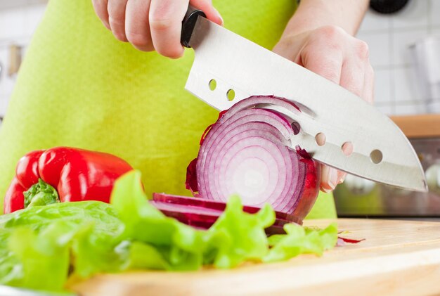 Le mani della donna che tagliano la cipolla del bulbo, dietro le verdure fresche.