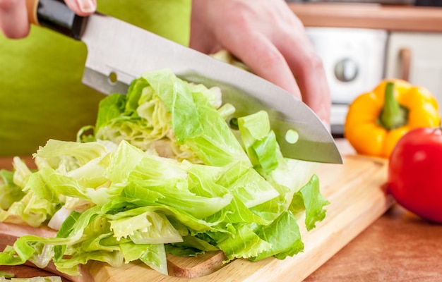 Le mani della donna che tagliano la lattuga, dietro le verdure fresche.