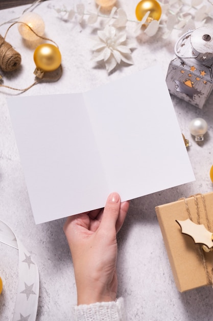 Le mani della donna che tengono la carta in bianco su fondo bianco. Design invernale natalizio. Mockup, vista dall'alto