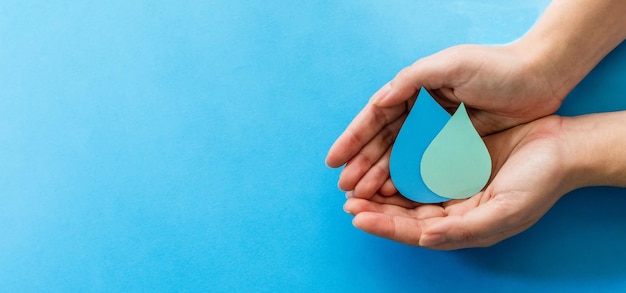 Le mani della donna che tengono la carta tagliano la goccia d'acqua su sfondo blu Acqua pulita e servizi igienico-sanitari risparmiando acqua Giornata mondiale dell'acqua Concetto di ecologia