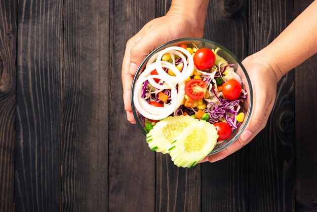 le mani della donna che tengono la sana insalatiera colorata con verdure miste fresche in un piatto