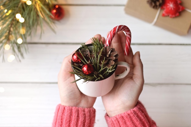 Le mani della donna che tengono la tazza con palloncini rossi, rami di albero di Natale e lecca-lecca Foto autentica