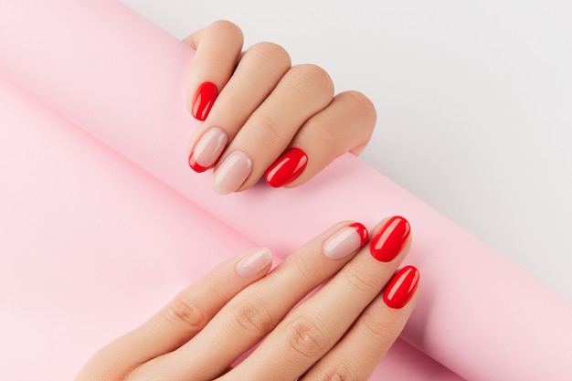 Le mani della donna con il manicure moderno rosso sopra le tendenze del design di manicure da parete bianca