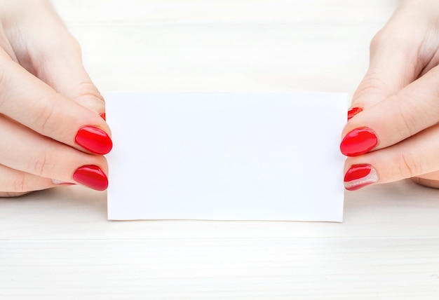 Le mani della donna con il manicure rosso che tiene il biglietto da visita su un tavolo di legno bianco