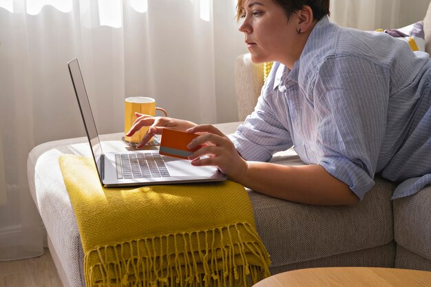 Le mani della donna con la carta di credito e l'utilizzo del computer portatile facendo acquisti online. Interni accoglienti in colori chiari durante la vendita dello shopping autunnale. Concetto di Black Friday e cyber Monday