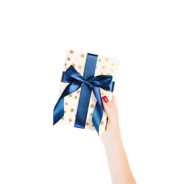 Le mani della donna danno il regalo fatto a mano di Natale o altra festa avvolto in carta dorata con il nastro blu