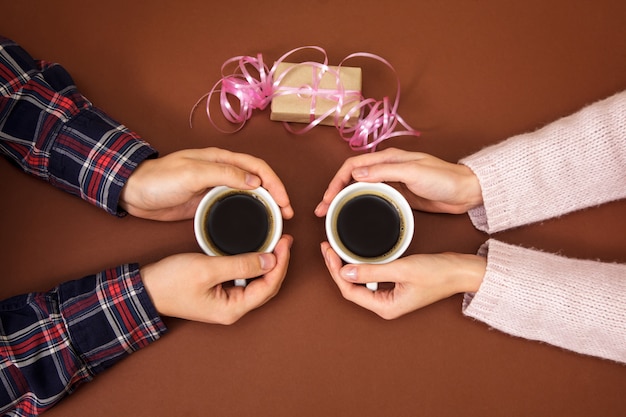 Le mani della donna e dell'uomo che tengono due tazze di caffè su marrone.