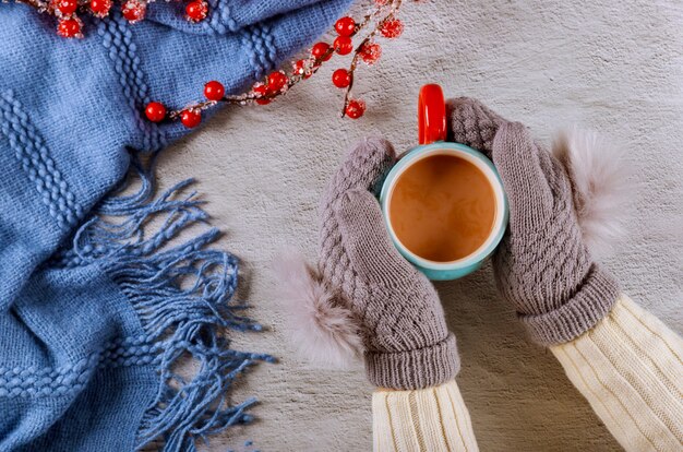 Le mani della donna in guanti di lana tricottati che tengono tazza di cacao caldo