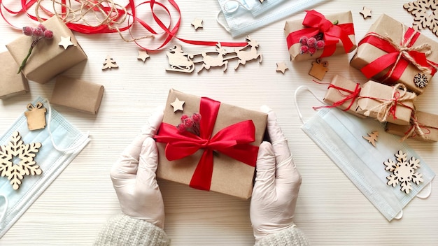 Le mani della donna in guanti medici tengono il regalo delle vacanze di Natale in carta artigianale con nastro rosso