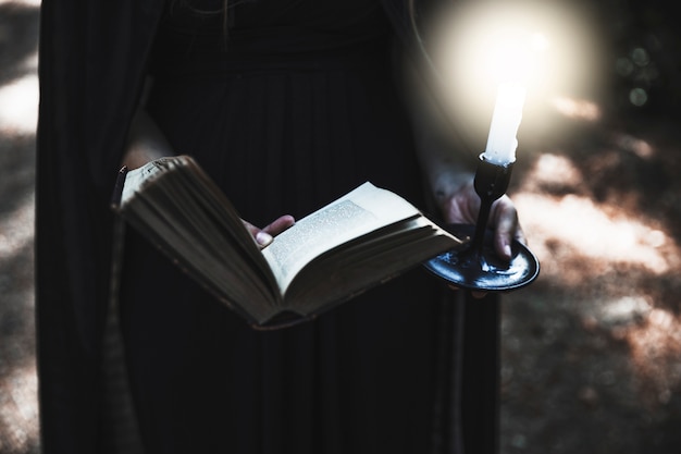 Le mani della donna in tenuta nera del vestito hanno aperto il libro e la candela bruciante