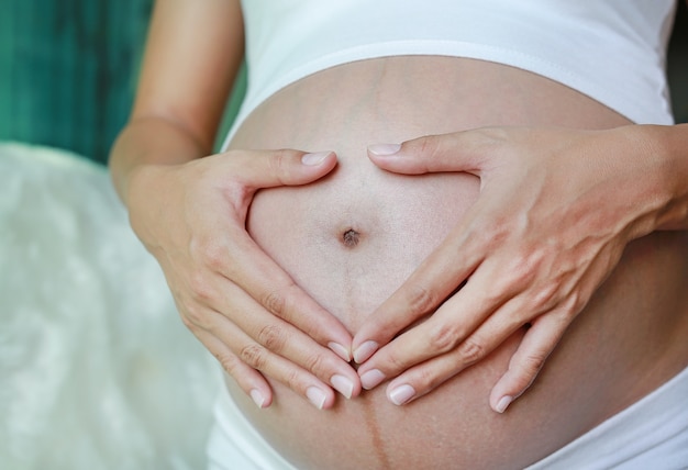 Le mani della donna incinta del primo piano a forma di cuore sulla sua pancia.