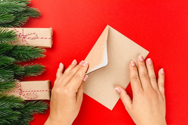 Le mani della donna inviano una lettera con gli auguri di Natale in una cornice di rami di abete e mazzetti di cannella.