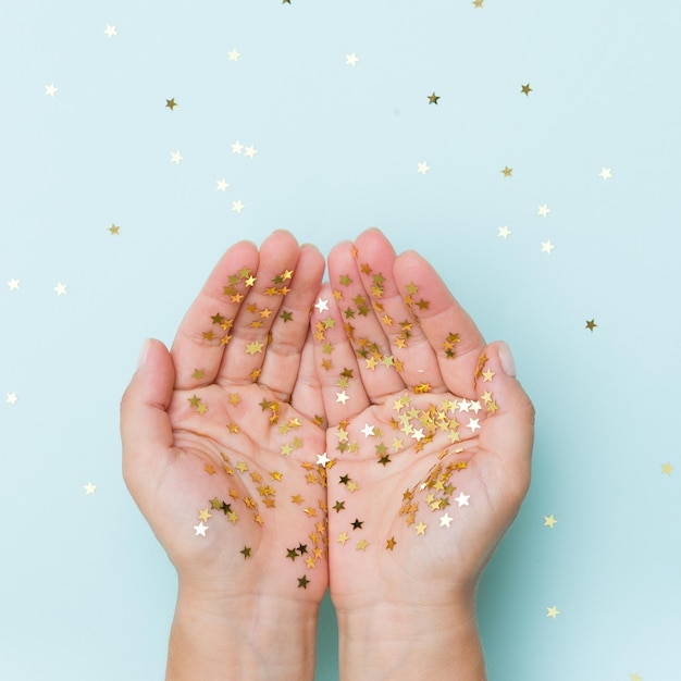 Le mani della donna ricoperte di coriandoli di stelle dorate su sfondo azzurro Concetto di Natale