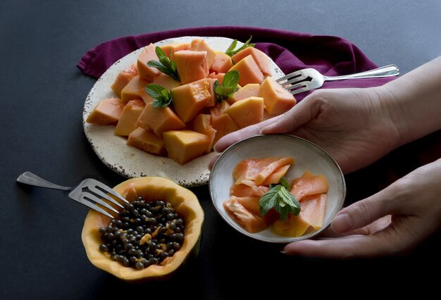 Le mani della donna servono piatti con frutta a fette di papaia sul piatto