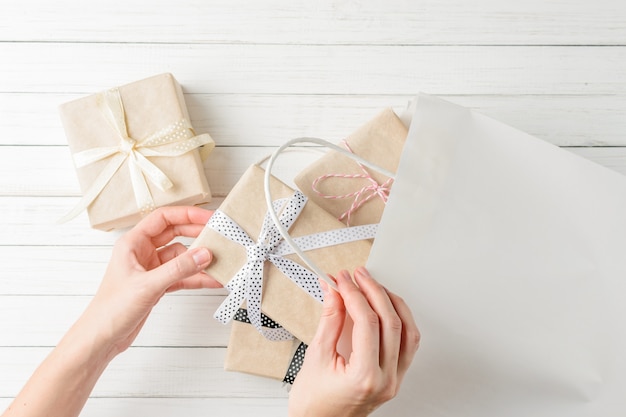 Le mani della donna stanno avvolgendo i presente in una borsa del regalo su fondo bianco, vista superiore