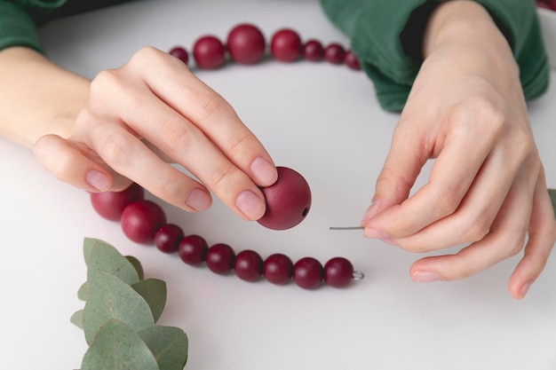 Le mani della donna stanno infilando perline di colore rosso su un filo Primo piano