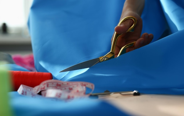 Le mani della donna tagliano il tessuto blu con il primo piano delle forbici su misura Sarto in atelier e sartoria