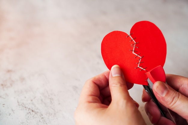 le mani della donna tengono il cuore spezzato rosso che fissa dalla cucitrice