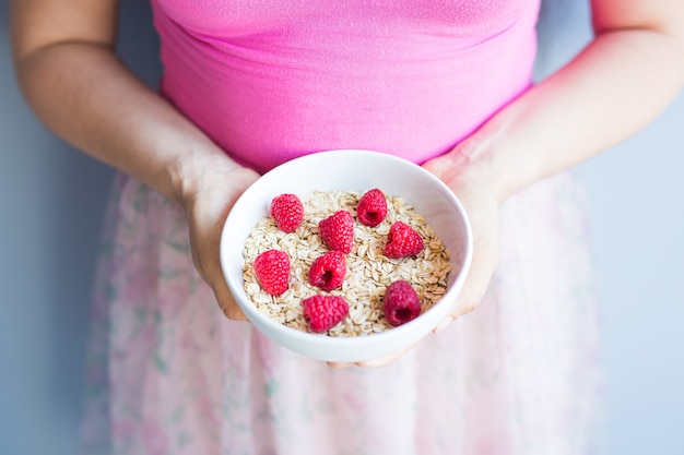 Le mani della donna tengono una colazione sana e naturale, farina d'avena e lamponi in una ciotola.