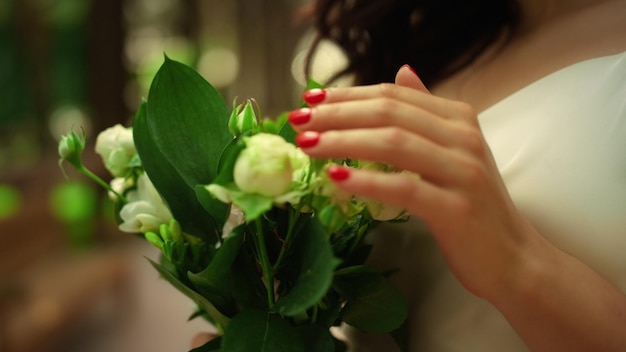 Le mani della donna toccano il bouquet nel parco Sposa in piedi con i fiori in giardino