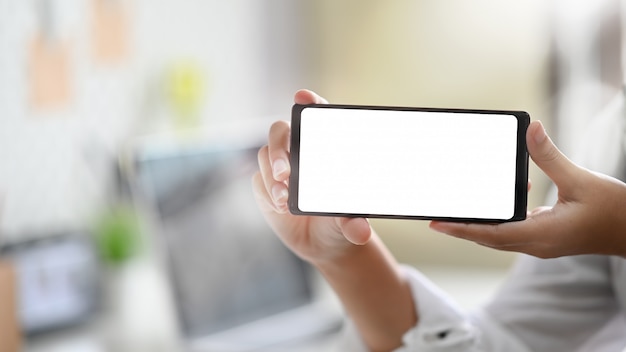 Le mani della femmina del primo piano che mostrano lo schermo in bianco del telefono cellulare.