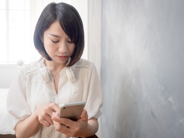 Le mani della giovane donna asiatica che tengono il telefono cellulare