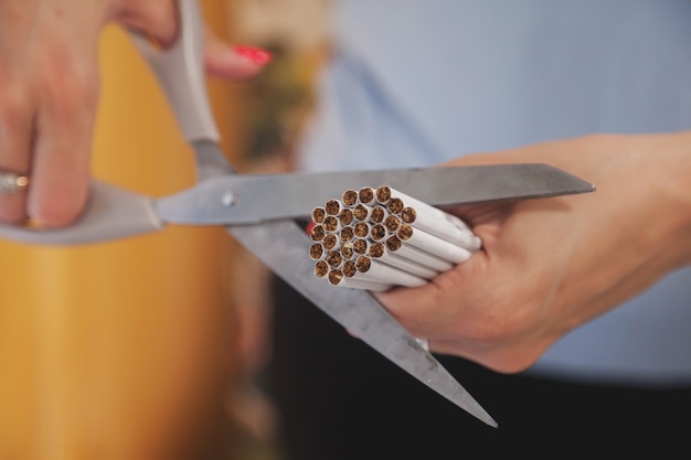 Le mani della giovane donna tagliano le sigarette con le forbici. Esci da Smok, combatti i tossicodipendenti da nicotina. Close-up di taglio a forbice sacco di sigaretta. Concetto di anti-fumo e stile di vita sano. Copia spazio