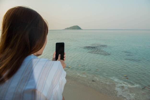 Le mani della giovane donna usano lo smartphone seduto su una roccia godendosi la spiaggia