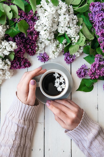 Le mani della ragazza con una tazza di caffè sul tavolo con fiori lilla distesi