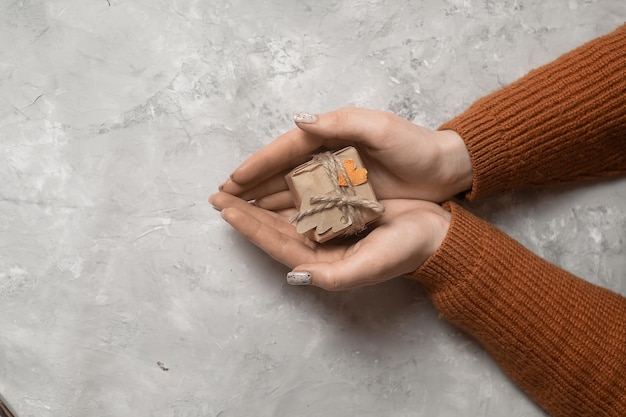 le mani della ragazza tengono un regalo avvolto in carta kraft tengono un regalo di Capodanno