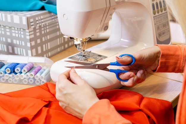 Le mani della sarta tagliano il filo della macchina da cucire, primo piano